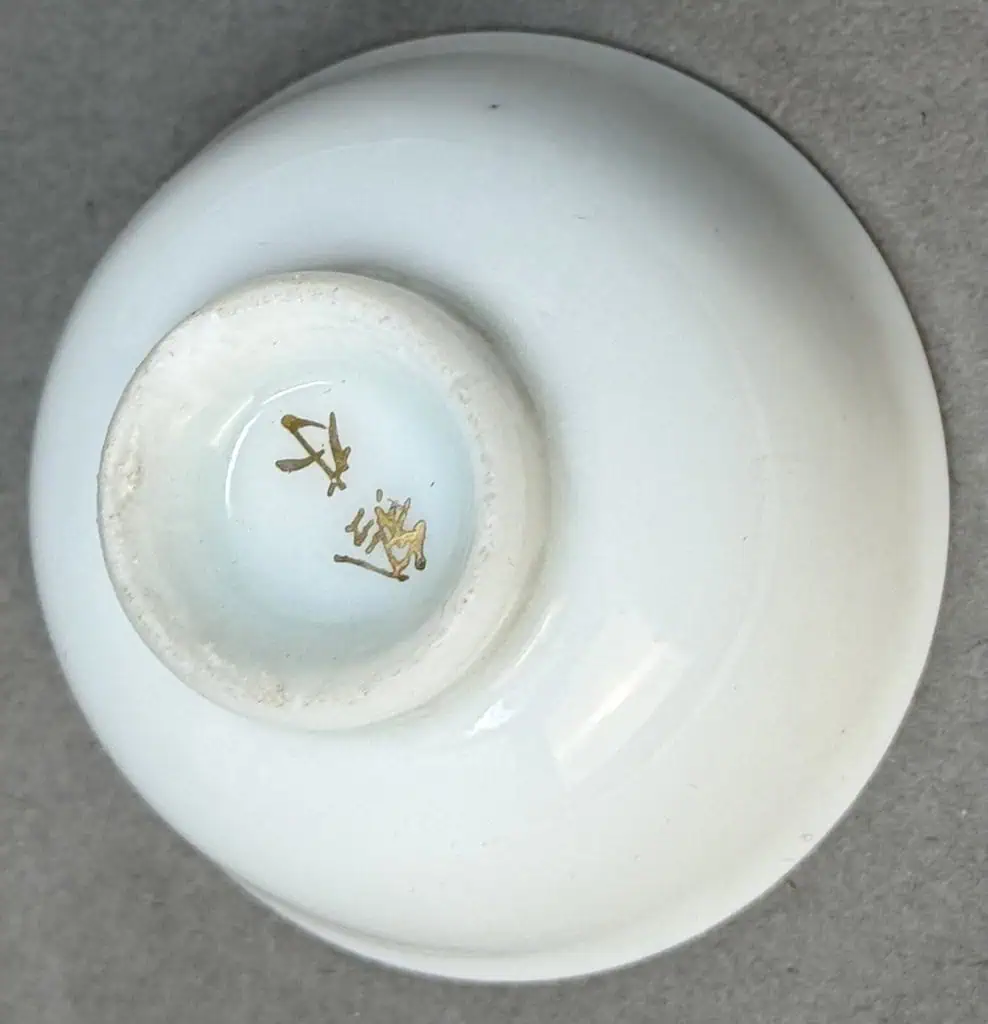Small ceramic dish with gold-colored symbols inside, on a gray surface.
