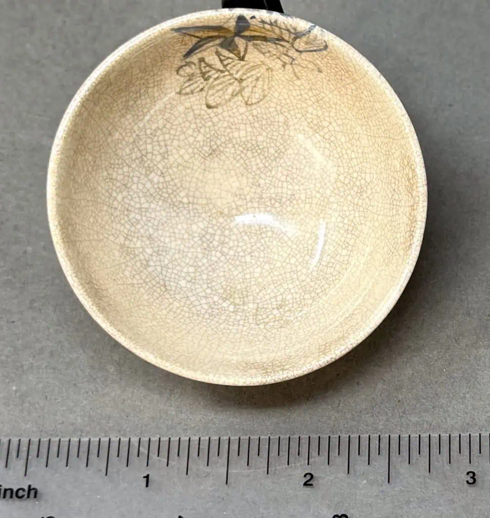 Antique ceramic bowl with crackle glaze and bird design at the rim, displayed on a gray surface.